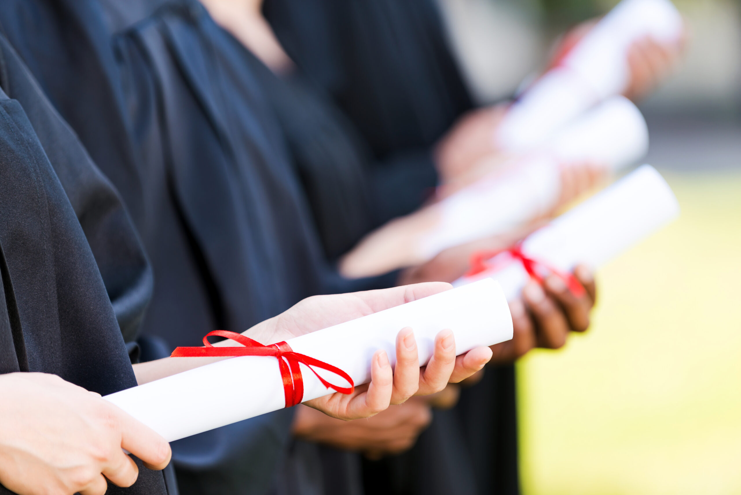 graduates with diplomas. close up of four college graduates standing in a row and holding their diplomas